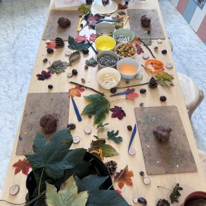 A craft table set up with natural materials like leaves, pinecones, and sticks, along with tools and clay for making hedgehog models