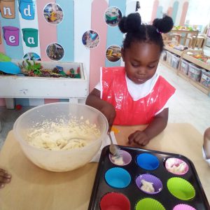 A child in a red apron filling colorful cupcake liners with batter during a baking activity.