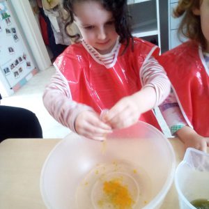 A child in a red apron cracking an egg into a mixing bowl during a baking activity.